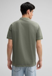 Olijfgroen polo-shirt van lichtgewicht stof, korte mouwen en een klassieke kraag. Losse pasvorm met een rechte zoom en minimale stikseldetails.