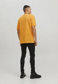 T-shirt di cotone arancione con vestibilità rilassata, maniche corte e scollo rotondo, abbinato a jeans skinny neri e stivali neri.