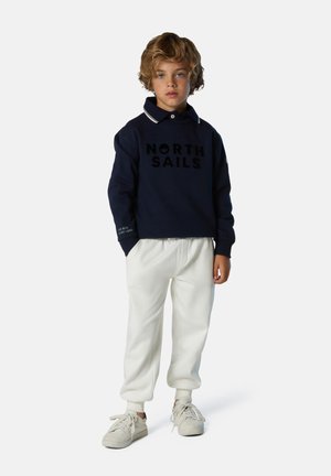 Dunkelblaues Sweatshirt mit "NORTH SAILS"-Logo, weißem Kragen und Bündchen, kombiniert mit weißen, lässigen Hosen und hellen Sneakers.