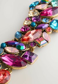 Farbiger Schmuckarmband mit verschiedenen geschliffenen Edelsteinen in Rosa, Lila, Blau und Goldtönen, mit komplizierten Anordnungen und Texturen.