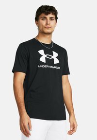 Melnā kokvilnas T-kreklā ir īsas piedurknes, apaļa kakla izgriezums un izteiksmīgs balts Under Armour logo uz priekšpuses. Gluda tekstūra.