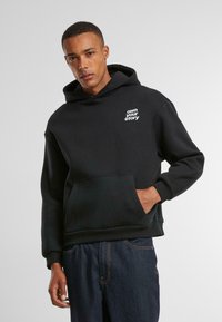 Schwarzer Kapuzenpullover aus weicher Baumwolle, mit einer Vorderasche und dem weißen Text "own your story" auf der linken Brustseite.