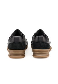 Des chaussures de sport noires avec une tige en cuir et daim, présentant une rayure d'accent blanche et une semelle en caoutchouc gomme. La vue arrière montre des surfaces lisses et texturées.