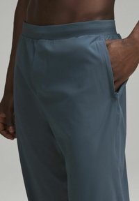 Lätta, mörkblå byxor med en slät textur, elastisk midja och sidfickor. Nära vy av midjan och fickområdet.