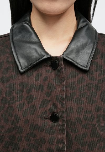 Prim-plan cu o persoană purtând o jachetă cu imprimeu leopard maro și negru, cu guler din piele neagră și nasturi negri închiși.