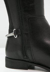 Botte en cuir noir hauteur genou avec une fermeture éclair sur le côté et des accents en métal argenté. Texture lisse avec un petit talon et un design simple.