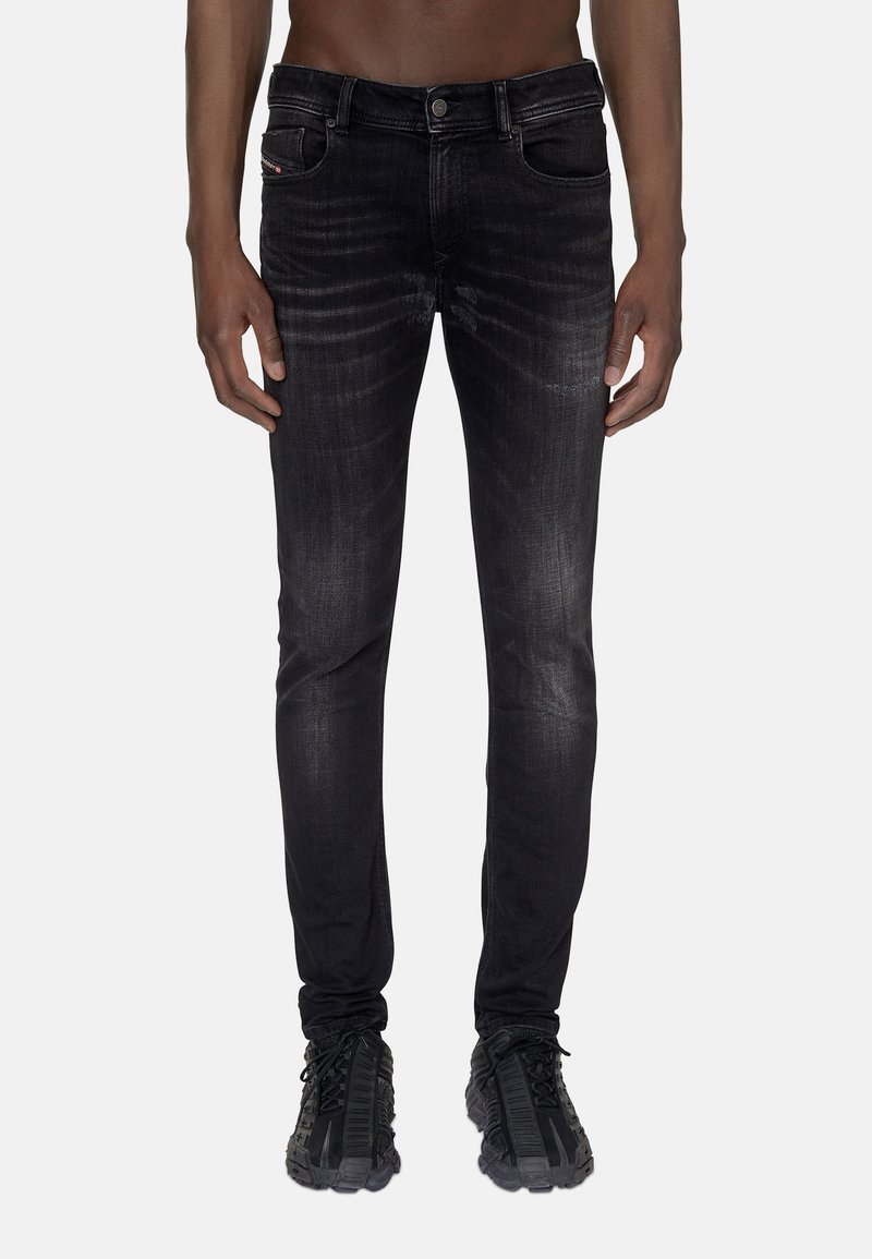 Jean en denim noir avec une coupe slim, présentant une texture délavée, un design à cinq poches et un logo discret sur la ceinture.