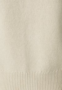 Tejido de punto color crema con una textura acanalada, que presenta un patrón suave y continuo y un dobladillo acanalado en la parte inferior.