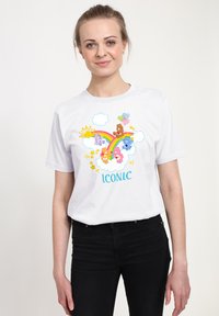 Bílé bavlněné tričko s barevnými karikaturami, včetně duhy, mraků a hvězd, se slovem "IKONICKÝ" v modrém písmu.