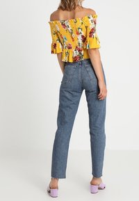 Top amarillo con flores, de hombros descubiertos y mangas con volantes, combinado con jeans de mezclilla de tiro alto y sandalias lavanda con tacón ancho.