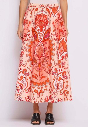 Gonna di lunghezza media con intricati motivi floreali e a paisley in rosa e arancione, indossata con pantofole nere intrecciate a punta aperta.