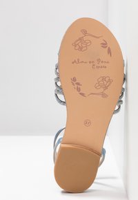Semelle de sandale avec motifs floraux, nom de marque "Alma en Pena Espana," et taille 37, montrant une partie des côtés supérieurs argentés à brides.