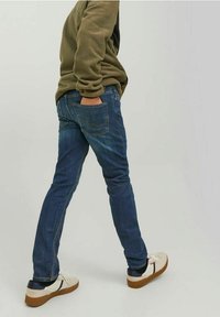 Tajta blå denimjeans med en klassisk femficksdesign, bärs med en beige fleece och vita sneakers med bruna detaljer.