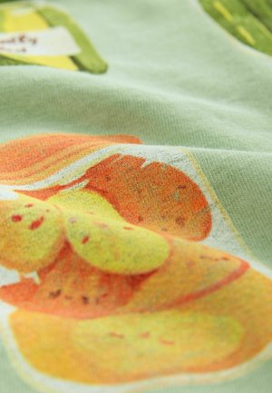 Le tissu en coton présente un motif de fruits ludique avec des oranges et des jaunes sur un fond vert clair, mettant en valeur une texture douce et des couleurs vibrantes.