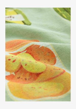 Baumwollstoff mit einem verspielten Fruchtmuster in Orange- und Gelbtönen auf einem hellgrünen Hintergrund, das eine weiche Textur und lebendige Farben zeigt.