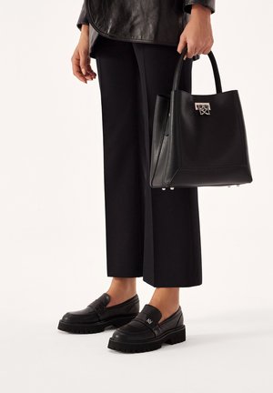 Person iført sort læderjakke og bukser, der holder en sort læderhåndtaske og bærer sorte loafers med chunky sål.