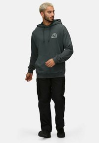 Sudadera gris oscuro con bolsillo frontal y un gráfico de calavera, combinada con pantalones cargo negros. Presenta cordones y puños de canalé.