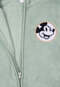 Giacca in fleece verde chiaro con zip, caratterizzata da una patch rotonda di Topolino sul lato sinistro. Tessuto morbido con zip a contrasto.