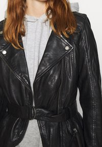 Czarna skórzana kurtka motocyklowa z paskiem w talii, zapinanymi na zamek kieszeniami i srebrnymi akcentami. Wewnętrzna warstwa wyposażona jest w szary nadruk.