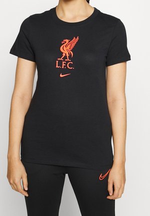 Kobieta nosząca czarną koszulkę Liverpool FC i legginsy z czerwonym logo klubu i znakiem Nike na piersi i udzie.