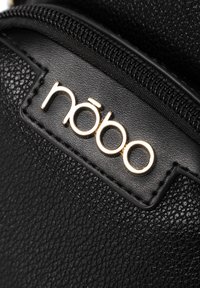 Borsa nera con texture e logo dorato. Presenta una cerniera e bordi lisci, evidenziando un design minimalista.