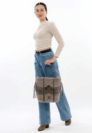 Grau strukturierte Handtasche aus flauschigem Material, mit einer glatten Vorderseite und Lederakzenten, getragen von einer Person in legerer Kleidung.