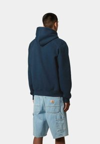 Sudadera azul marino con una capucha grande, puños acanalados, combinada con pantalones cortos de mezclilla azul claro tipo cargo con bolsillos y un parche de logo en la parte trasera.