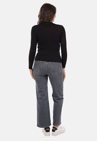 Top nero a costine con maniche lunghe e design aderente, abbinato a jeans grigi a gamba dritta e sneakers bianche con dettagli neri.