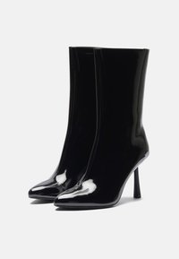 Crne lakirane gležnjače s elegantnim, prilagođenim dizajnom, šiljastim nosom i visokim potpeticama u obliku stiletto. Glatka, sjajna tekstura kroz cijeli model.