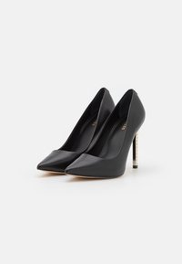 Chaussures à talons hauts en cuir noir avec un design pointu et un talon orné d'un accent métallique. Texture lisse, style minimaliste, et silhouette élégante.