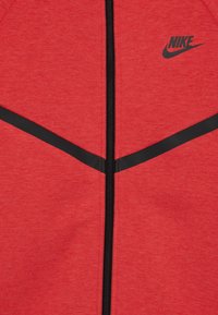 Giacca zip-up rossa Nike con una texture morbida, chiusura con zip nera e accenti neri in contrasto sul petto. Logo sul lato sinistro.