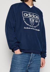 Mörkblå tröja med rund hals och vit adidas-logotyp och text. Har en avslappnad passform, ribbade ärmslut och rund halsringning.