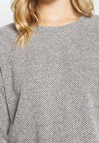 Grå stickad tröja med ett texturerat mönster, rund urringning och avslappnad passform. Tyget har ett mjukt och mysigt utseende.