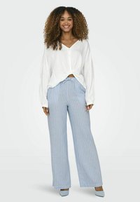 Witte overhemdd met een geknoopte voorkant, gecombineerd met lichtblauwe gestreepte wijde broek. De outfit is gemaakt van zachte stof en heeft een relaxte pasvorm.