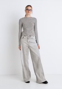 Ριγέ μακρυμάνικη μπλούζα σε λευκό και μαύρο, συνδυασμένη με ανοιχτό γκρι τζιν παντελόνι με φαρδιές μπατζάκια. Λείο ύφασμα με εμφανείς τσέπες και άνετη εφαρμογή.