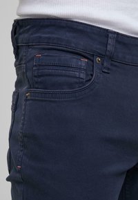 Námořnické modré džíny mají slim-fit design s jemnými švy, předními kapsami a hladkou texturou.