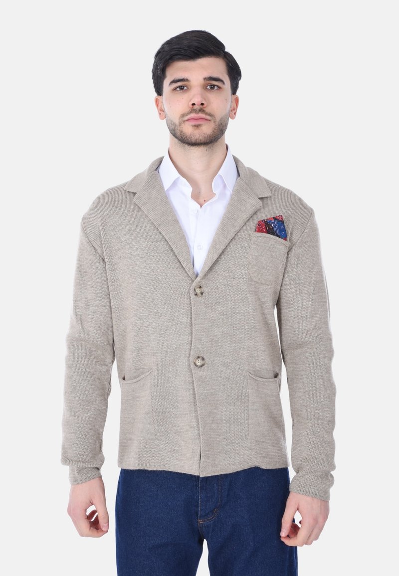 Cardigan beige a maglia con collo a scialle, due tasche frontali e un fazzoletto decorativo a fantasia. Bottoni frontali, maniche lunghe.