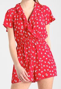 Jumpsuit floral rojo con mangas cortas, que presenta un diseño cruzado, cintura elástica, patrones de flores en blanco y negro, y dobladillo festoneado.