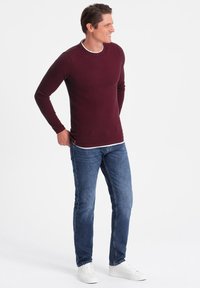 Burgundy knit long-sleeve shirt with a white accent at the collar, paired with blue denim jeans and white sneakers. Casual fit and textured fabric.