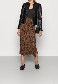 Giacca di pelle nera, canotta nera, gonna midi in stampa leopardata marrone con spacco laterale e mocassini neri. Inclusa borsa a tracolla regolabile.