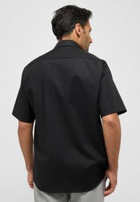 Maglietta nera a maniche corte con una texture morbida e colletto a punta, caratterizzata da un taglio pulito e affusolato e orlo curvo sul retro.