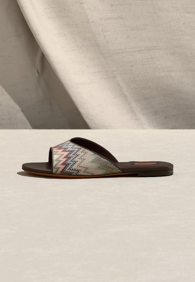 Sandale plate à glissière avec tige en tissu à motif zigzag aux couleurs pastel sur un fond neutre.