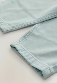 Helles blaugraues Denim-Gewebe mit feiner Struktur, versehen mit umgeschlagenen Säumen und kontrastierenden gelben Nähten an den Kanten.