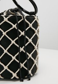 Czarna skórzana torebka z białym wzorem z siatki z lin, z trokami i czarnymi okrągłymi uchwytami. Teksturalna powierzchnia z diamentowymi wzorami.