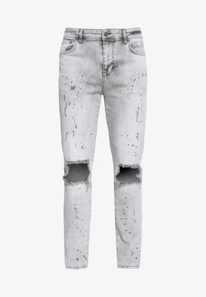 Světlé šedé skinny džíny s roztrhanými koleny a černobílými fleky barvy na přední části.