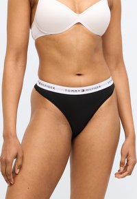 Fekete pamut tangában fehér elasztikus derékpánttal, amelyen a "TOMMY HILFIGER" felirat szerepel. A design minimalista és testhezálló.