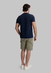 T-shirt blu navy a maniche corte abbinato a pantaloni cargo verde oliva, con tasche laterali. Le scarpe sono bianche con una texture liscia.