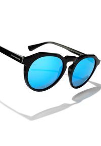 Černé sluneční brýle s geometrickým rámem, modrými reflexními čočkami a jemným logem na stranicích. Rovné nožičky se směrem ke konci zužují.