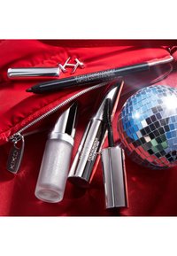 Una bolsa roja brillante contiene un frasco de spray plateado, un lápiz de delineador negro, un tubo de máscara de pestañas plateado y un adorno de bola de discoteca.