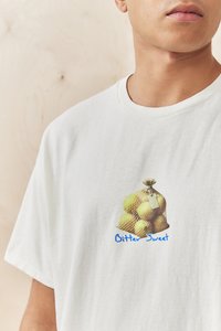 White cotton T-shirt featuring a graphic of a mesh bag with yellow apples and the text "Bitter Sweet" in blue below the image.